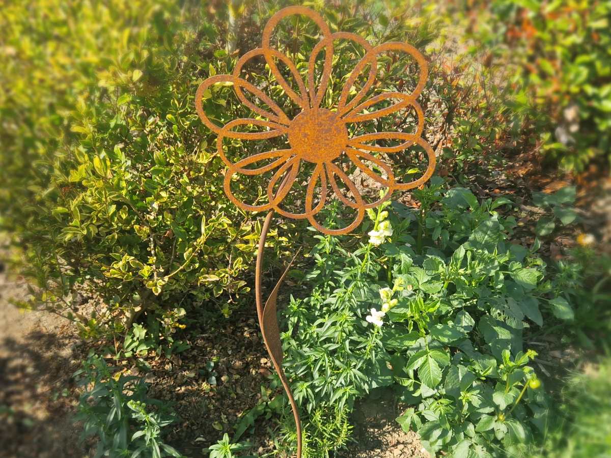 Rostiger Blumen-Gartenstecker mit geschwungenem Stiel zwischen grünen Pflanzen im Beet